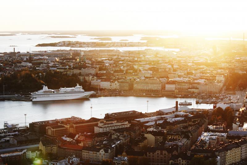Auringonnousu satamassa Helsingissä. Satamassa iso risteilijä ja pienempiä veneitä.