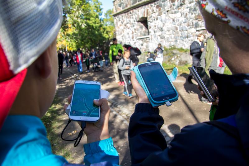 Nuoret pelaavat kännyköillä Suomenlinnassa kesäisenä päivänä.