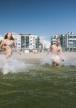 Aurinkolahden uimarannalla veteen juoksee kaksi naista ja yksi mies.